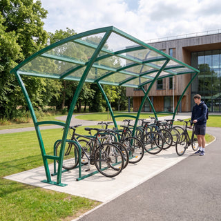 Armstrong 20 cycle bike shelter in Traffic Green on a leafy university campus path with bicycles parked