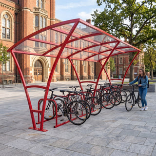 Armstrong 20 cycle bike shelter in Traffic Red beside a historic red-brick university building with bicycles parked