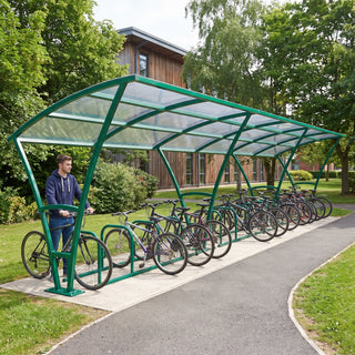 Armstrong 30 cycle bike shelter in Traffic Green on a leafy university campus path with bicycles parked