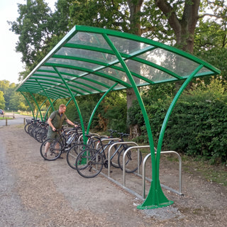 Armstrong CHS 24 cycle curved bike shelter in Traffic Green at a UK country park with a cyclist parking his bike
