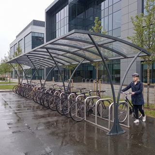 Armstrong CHS 24 cycle curved bike shelter in Anthracite Grey at a UK business park with a commuter arriving by bike