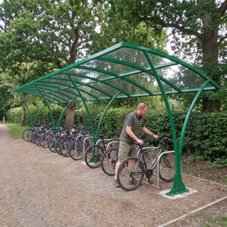 Armstrong CHS 30 cycle curved bike shelter in Traffic Green at a UK country park with a cyclist parking his bike