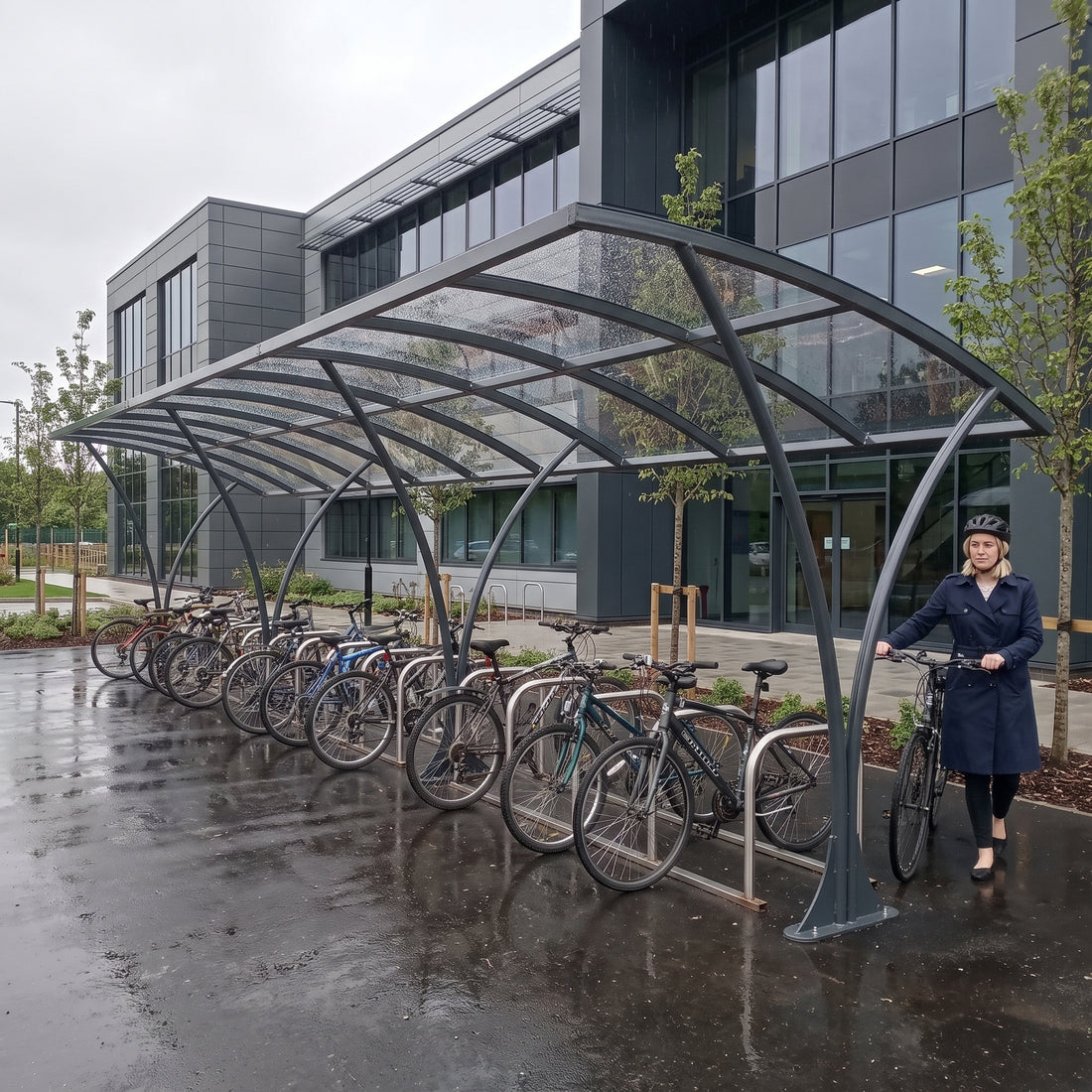Armstrong CHS 30 cycle curved bike shelter in Anthracite Grey at a UK business park with a commuter arriving by bike