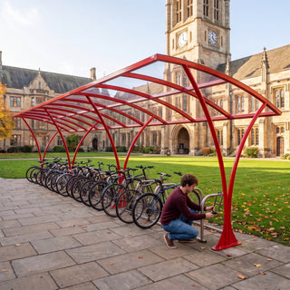 Armstrong CHS 30 cycle curved bike shelter in Traffic Red in a UK university quad with a student locking his bike