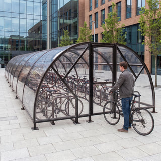 Black 100 cycle bike shelter (Salisbury Closed Compound SAL100CC) on a university campus plaza with a student and bicycle at the gate